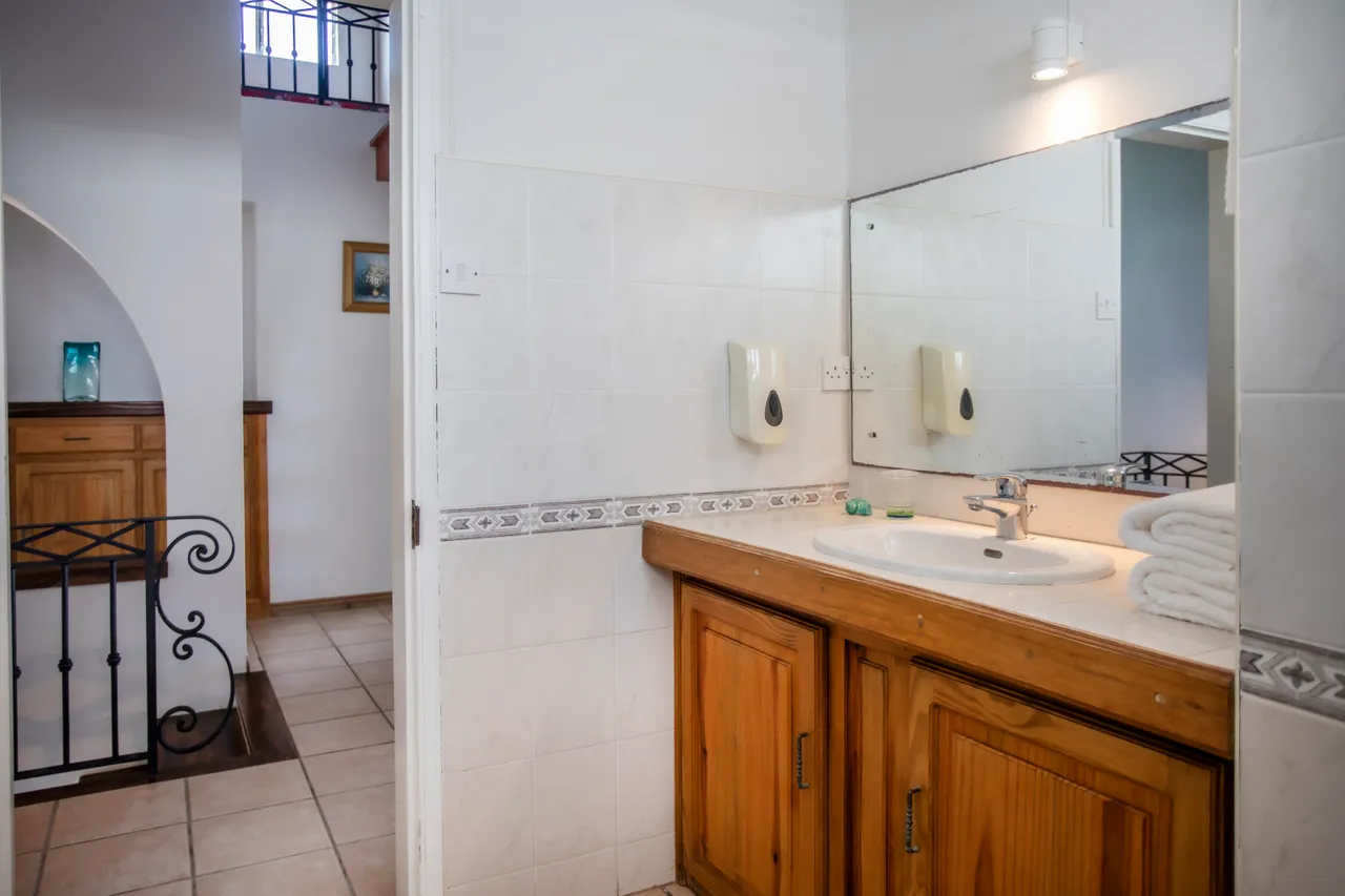 Salle de bains. Lavabo en bois avec miroir et rangements. Carrelage clair au sol.
