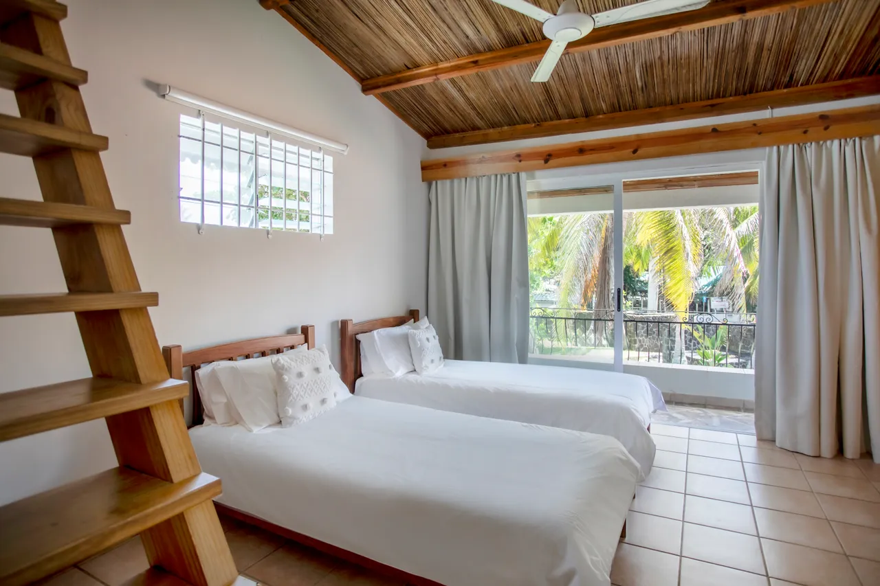 Chambre avec deux lits simples et fenêtres donnant sur l'extérieur. Plafond en bois et carrelage au sol.