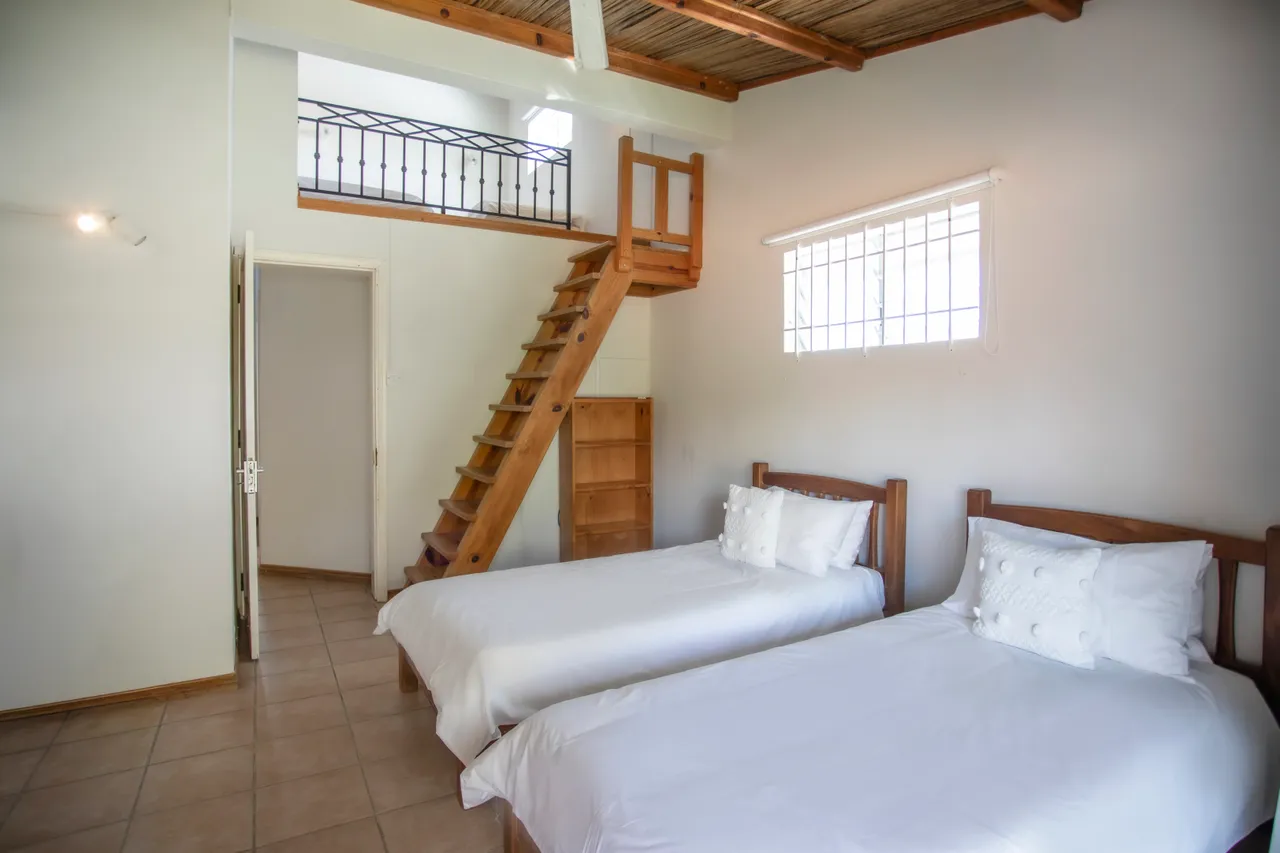 Chambre avec deux lits simples et plafond en bois. Sol en carrelage clair. Éclairage naturel par la fenêtre. Rangements intégrés en bois.
