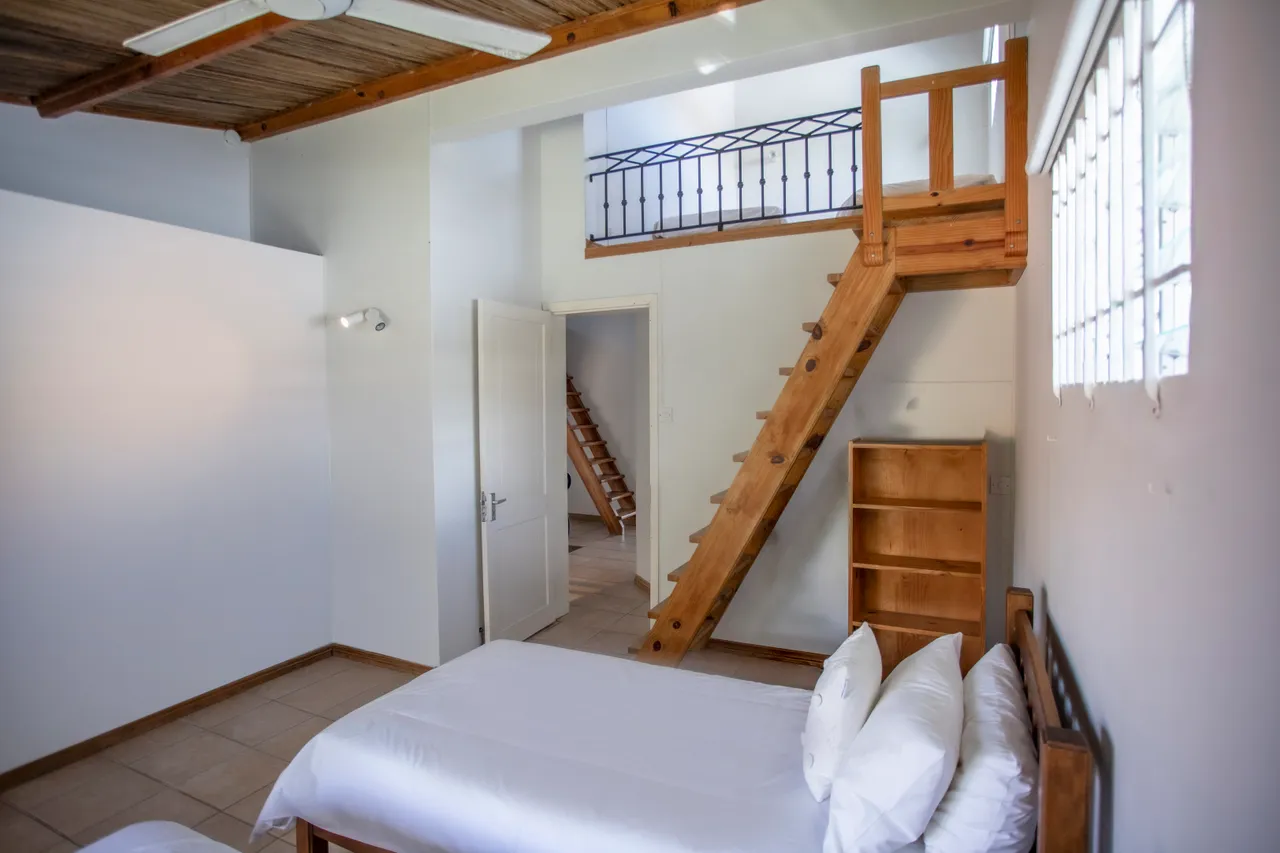 Chambre avec lits simples et fenêtres offrant une vue sur l'extérieur. Plafond en bois et rangements intégrés en bois. Escaliers en bois menant à un espace supérieur.