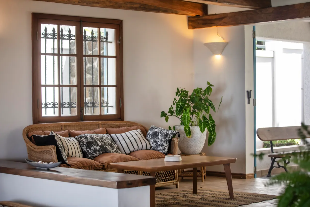 Espace de détente avec canapé en rotin et coussins. Lumière naturelle par les fenêtres.