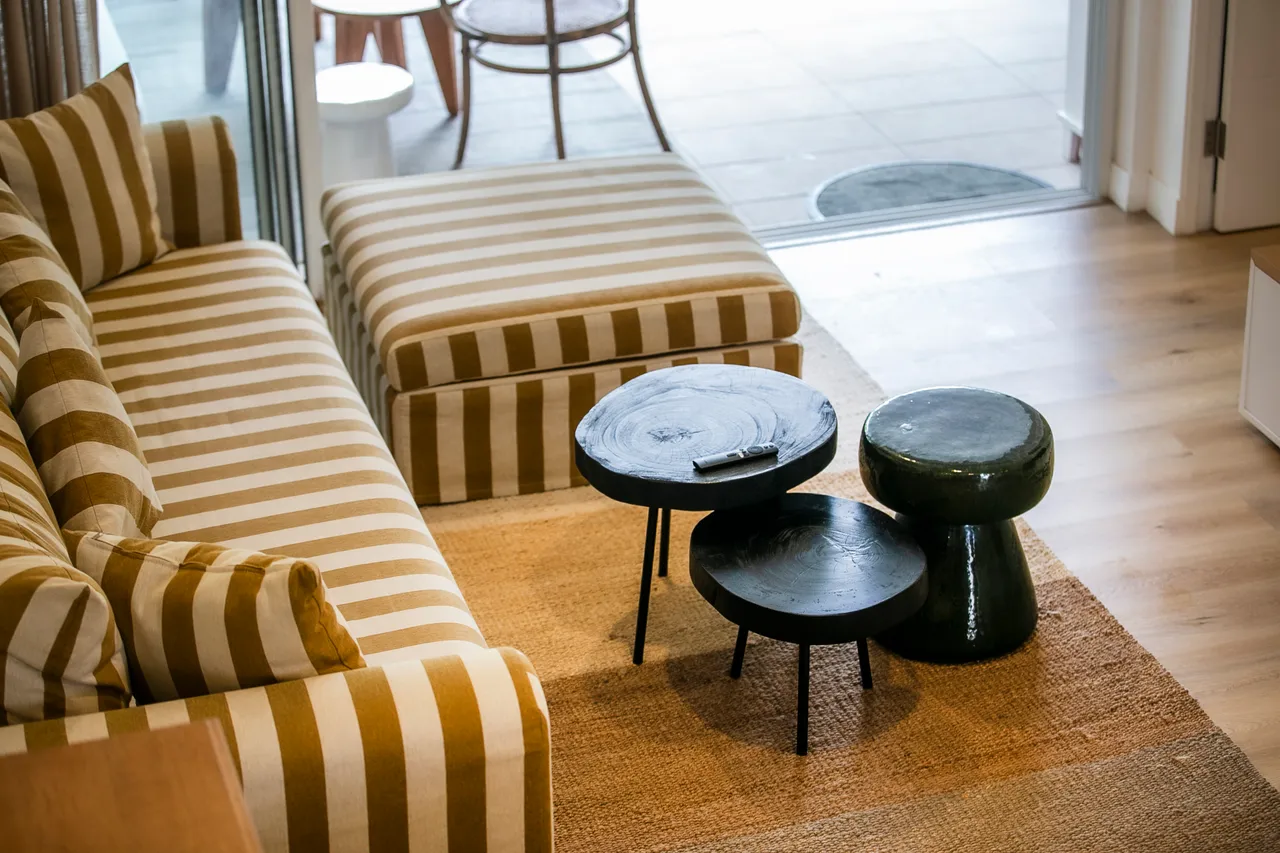 Canapé à rayures avec pouf assorti pour un espace de détente.  
Tables basses aux formes organiques en contraste avec le sol clair.
