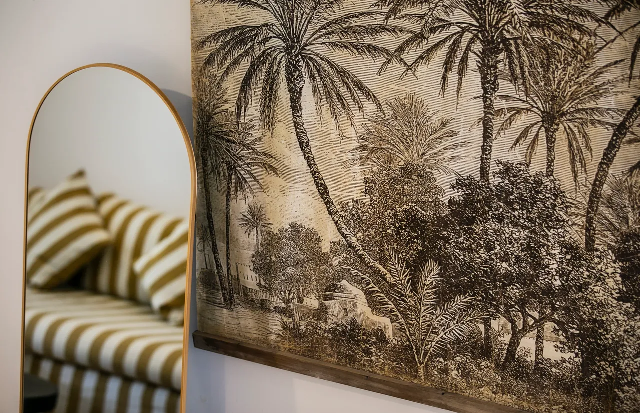 Tons terreux sur le mur et les motifs de l'œuvre d'art.  
Miroir arrondi reflétant la lumière et agrandissant l'espace.  
Coussins à rayures sur le canapé ajoutent une touche de texture.   
Détails végétaux dans la décoration renforcent une ambiance naturelle.  
Éléments en bois apportant chaleur et authenticité à la