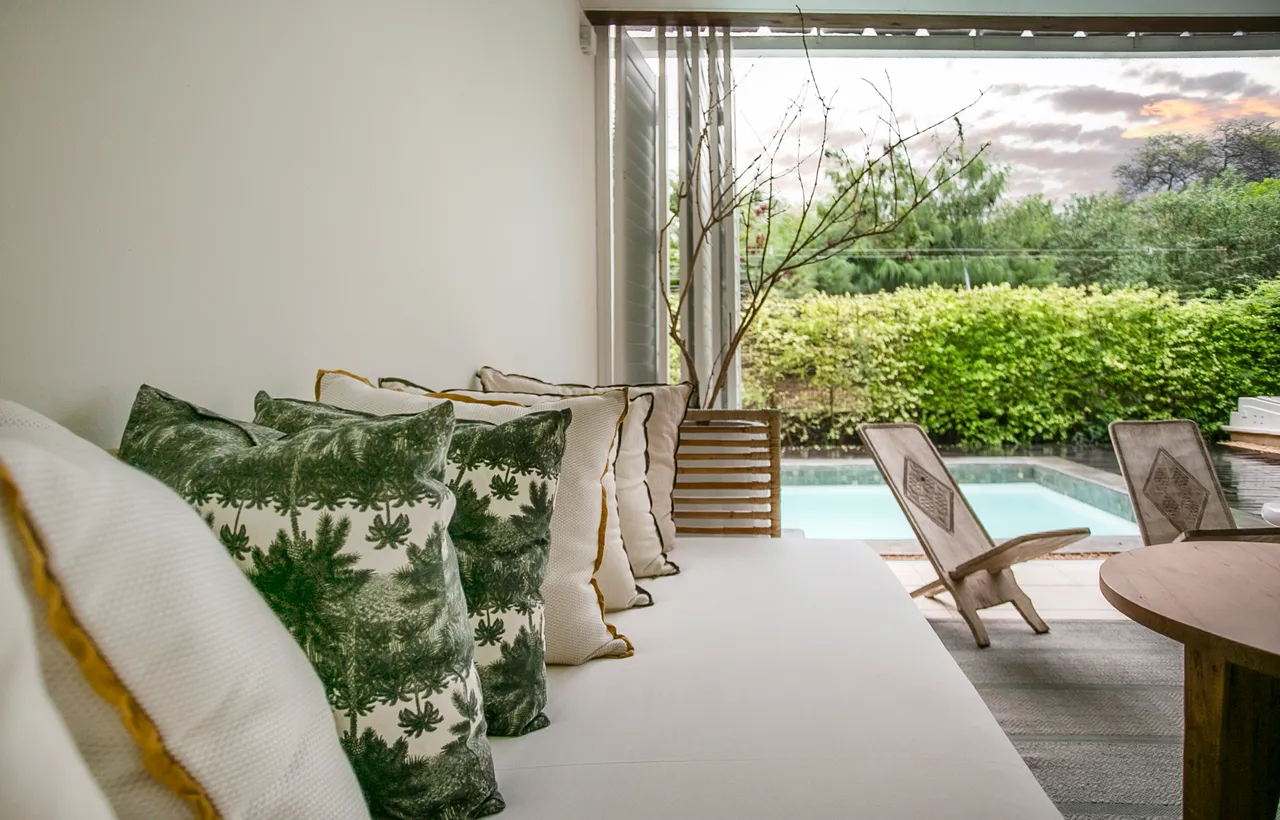 Tons verts des coussins apportent une touche naturelle à l'espace.  
Mobilier en bois clair créant un coin détente près de la piscine.  
Végétation environnante renforce l'intimité tout en embellissant l'espace.  
Lumière douce filtrant à travers les fenêtres, ajoutant une ambiance sereine.  
Sol en textile tissé offrant confort et chaleur à l