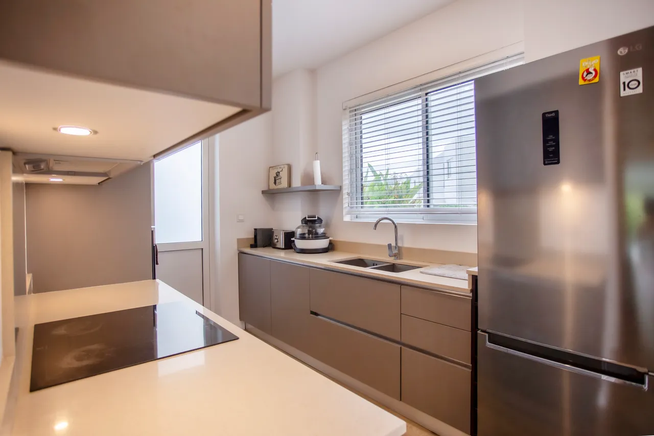 Cuisine équipée avec plans de travail en quartz et rangement intégré.  
Fenêtre laissant entrer la lumière naturelle, éclairant l’espace de travail.  
Appareils électroménagers modernes facilitant la préparation des repas.  
Éclairage sous les meubles créant une ambiance fonctionnelle.  
Agencement épuré maximisant l'espace disponible pour cuisiner.