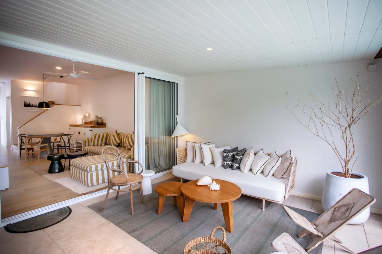 Lumière naturelle provenant des fenêtres créant une atmosphère lumineuse.  
Canapé en tissu clair apportant confort à l'espace de vie.  
Table basse en bois ronde ajoutant une touche chaleureuse au décor.  
Espace ouvert sur le salon et salle à manger, favorisant la circulation.  
Vues sur l'extérieur à travers les baies vitrées.