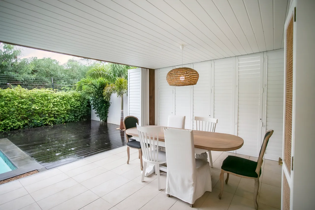 Terrasse lumineuse dotée d'une table ronde et de chaises pour les repas.  
Grandes baies vitrées ouvrant sur l'extérieur et la piscine.  
Plantes vertes offrant une ambiance naturelle et apaisante.  
Sol carrelé facilitant l'entretien de l'espace.  
Éclairage suspendu en osier ajoutant une touche chaleureuse.