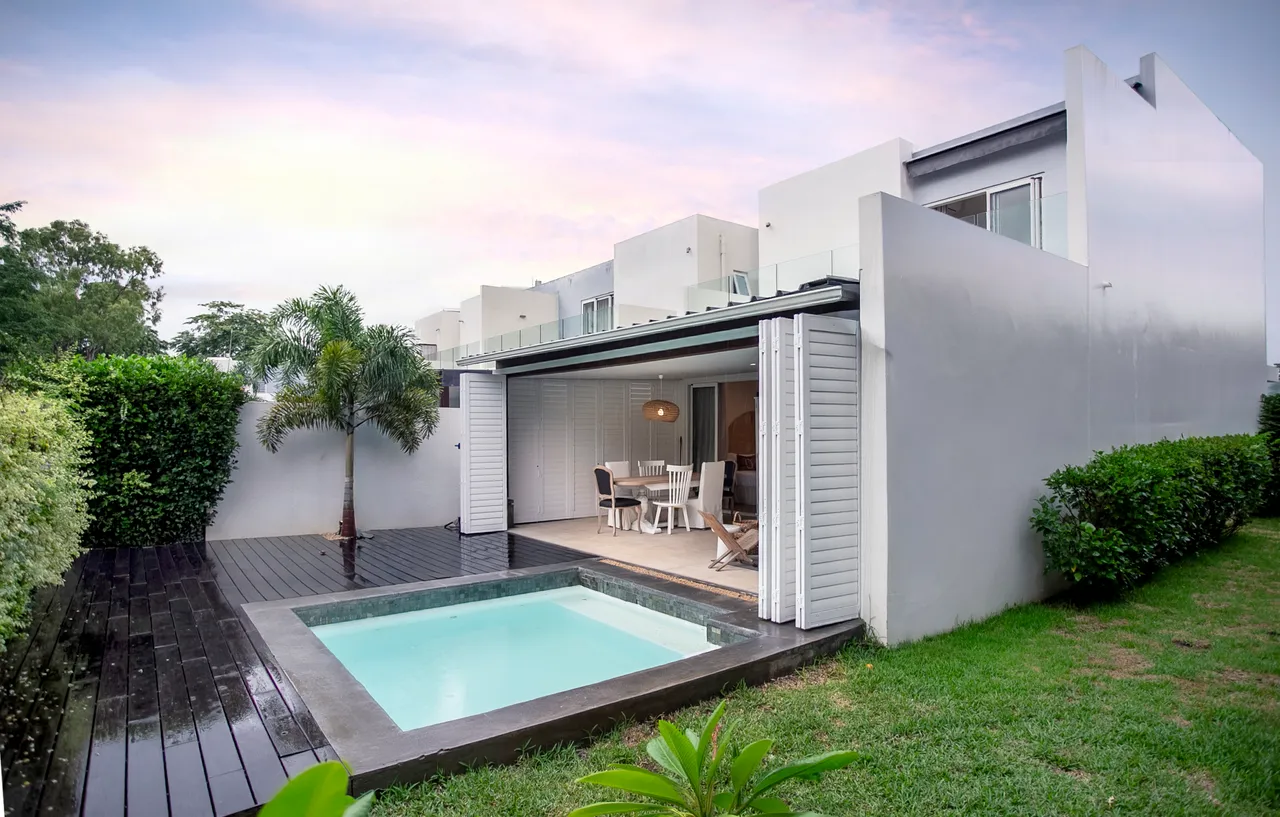 Ouverture sur l'extérieur grâce à des baies vitrées coulissantes.  
Espace piscine adjacent à une terrasse en bois pour des moments de détente.  
Mobilier de jardin simple offrant un cadre fonctionnel pour les repas.  
Végétation soigneusement entretenue ajoutant de la verdure au jardin.  
Coin repas extérieur pour profiter de l'air frais en toute tranquillité.