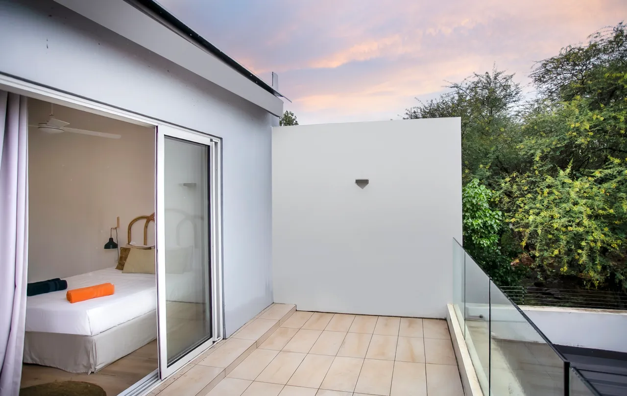 Balcon privé avec vue sur la végétation environnante.  
Porte-fenêtres offrant un accès direct depuis la chambre.  
Sol carrelé garantissant un espace extérieur facile d'entretien.  
Ambiance calme et sereine grâce à la verdure adjacente.  
Éclairage naturel grâce à l'orientation du balcon.