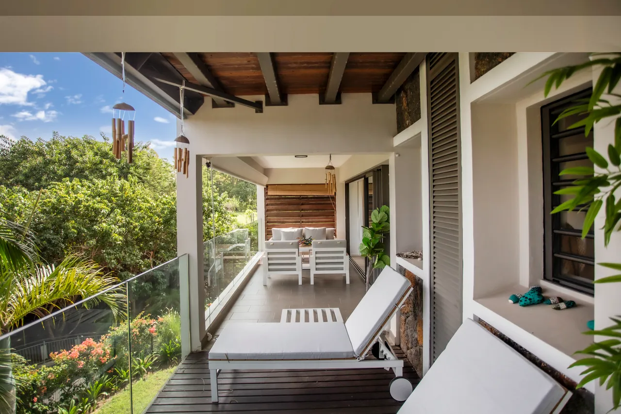 Espace extérieur avec chaises longues et vue sur le jardin.  
Balustrade en verre offrant un accès dégagé à la nature environnante.  
Terrasse couverte avec coin repas idéal pour se détendre.  
Plantes vertes ajoutant une touche naturelle à l'espace extérieur.  
Éclairage chaleureux créant une ambiance agréable sur la terrasse.
