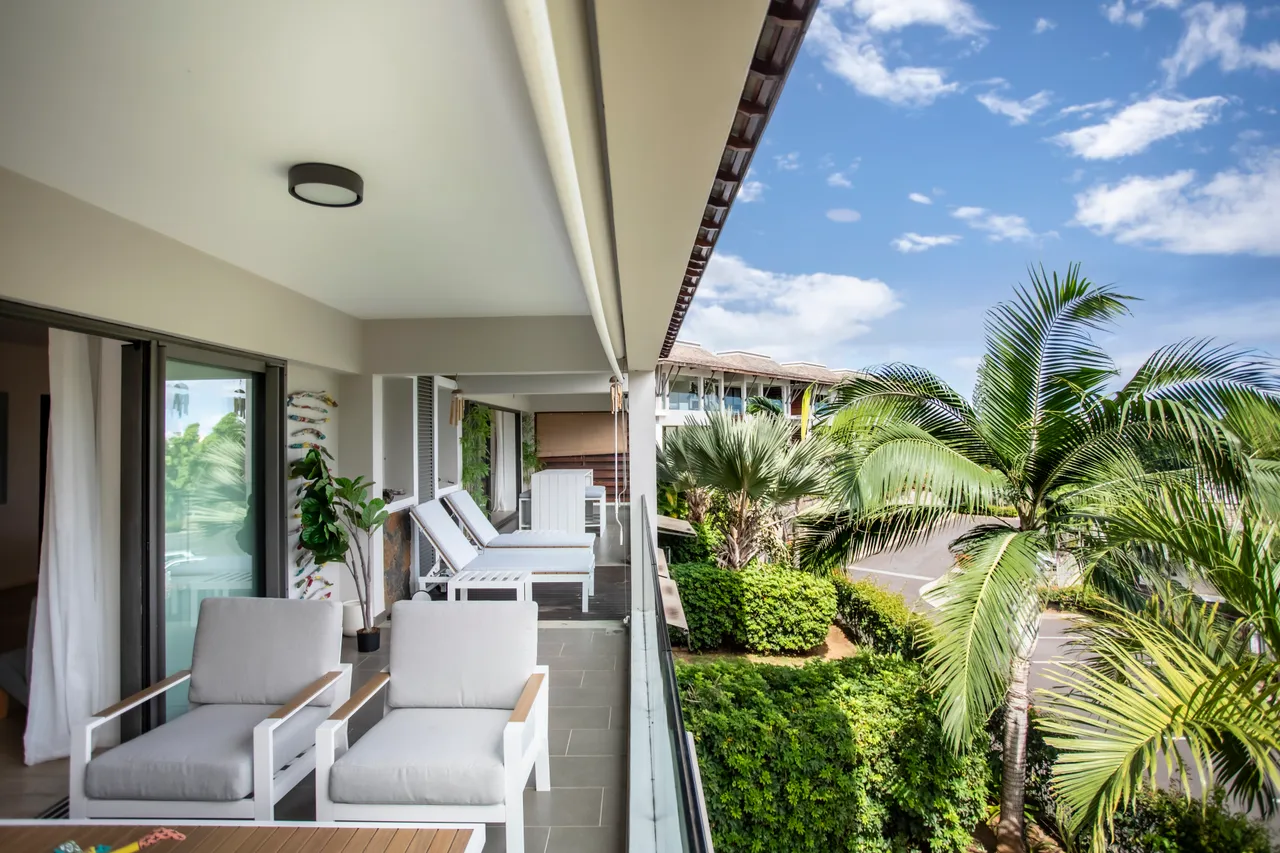 Couleurs neutres des meubles créant une ambiance apaisante sur la terrasse.  
Mobilier moderne avec chaises longues offrant un espace de détente extérieur.  
Végétation environnante ajoutant une dimension naturelle à l'espace.  
Terrasse spacieuse avec accès direct aux espaces de vie intérieurs.  
Vue dégagée sur le jardin et palmiers depuis l'espace extérieur.