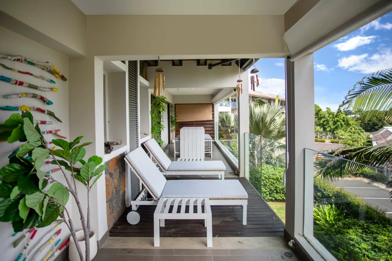 Espace extérieur avec chaises longues et vue sur le jardin luxuriant.  
Balustrade en verre offrant une vue dégagée sur l'environnement.  
Terrasse spacieuse avec accès direct depuis les pièces intérieures.  
Plantes vertes ajoutant une touche naturelle à l'espace extérieur.  
Éclairage naturel grâce aux grandes fenêtres laissant entrer la lumière.