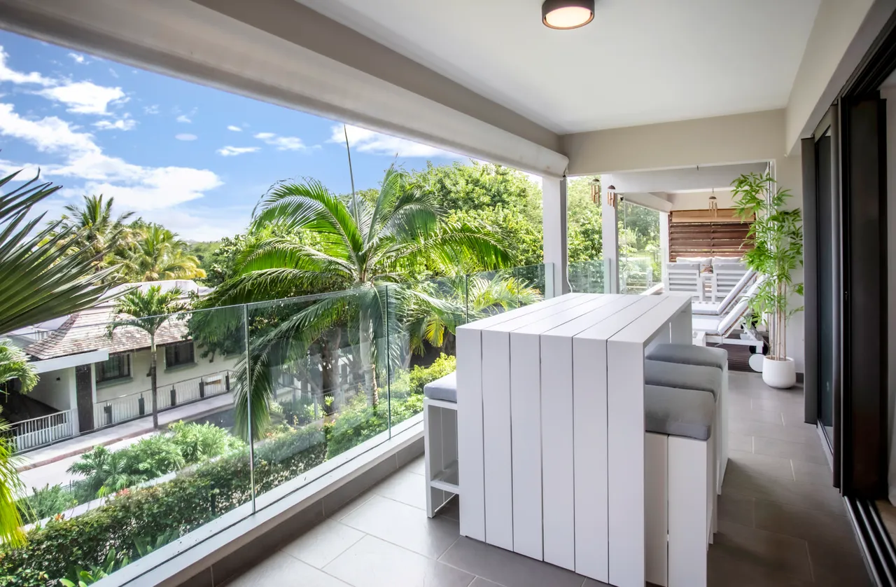 Mobilier en bois clair sur la terrasse offrant une vue dégagée.  
Végétation luxuriante visible à travers la balustrade en verre.  
Espace extérieur lumineux avec éclairage naturel abondant.  
Coin repas pratique sur la terrasse pour des repas en plein air.  
Accès facile depuis l'intérieur, permettant une circulation fluide.