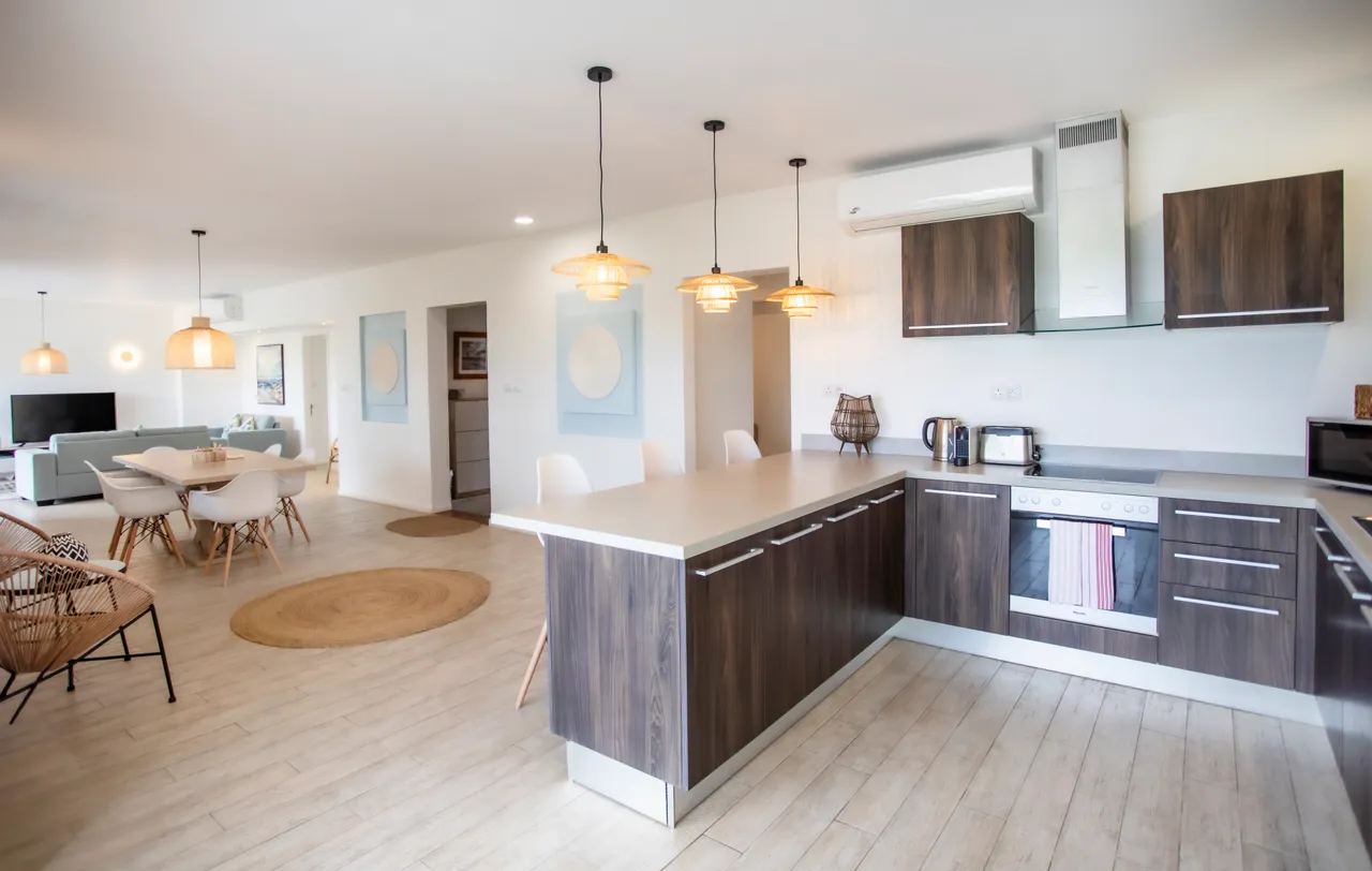 Cuisine équipée avec mobilier contemporain et plan de travail spacieux.  
Éclairage suspendu ajoutant une touche chaleureuse à l'espace de vie.  
Salle à manger attenante, facilitant les repas conviviaux en intérieur.  
Floors en bois clair offrant une atmosphère lumineuse et accueillante.  
Accès direct au salon depuis la cuisine, favorisant la fluidité des mouvements.