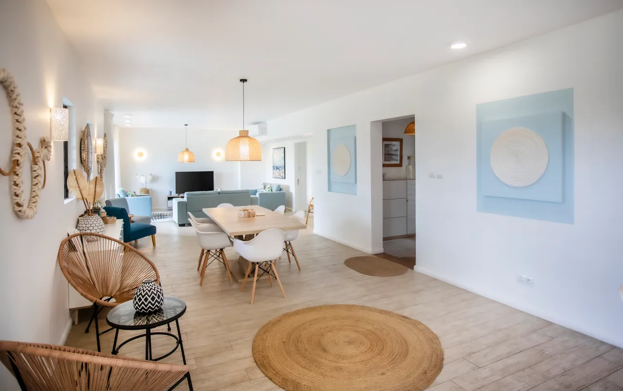 Espace de vie ouvert avec un éclairage naturel abondant.  
Mobilier moderne en bois clair ajoutant une touche contemporaine.  
Sol en bois clair créant une ambiance chaleureuse et lumineuse.  
Coin repas intégré favorisant des moments conviviaux en intérieur.  
Décor sobre avec touches artistiques apportant du caractère à l'espace.