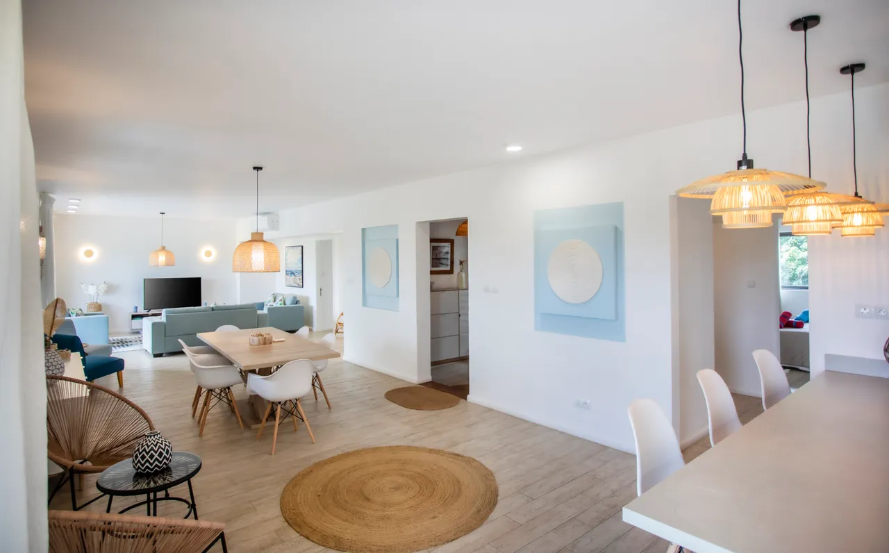 Espace de vie ouvert avec salon et salle à manger bien agencés.  
Mobilier contemporain et éclairage suspendu créant une ambiance moderne.  
Cuisine intégrée avec bar pour des repas informels et conviviaux.  
Sol en carrelage clair facilitant l'entretien et apportant luminosité.  
Fenêtres larges laissant entrer la lumière naturelle dans l'espace.