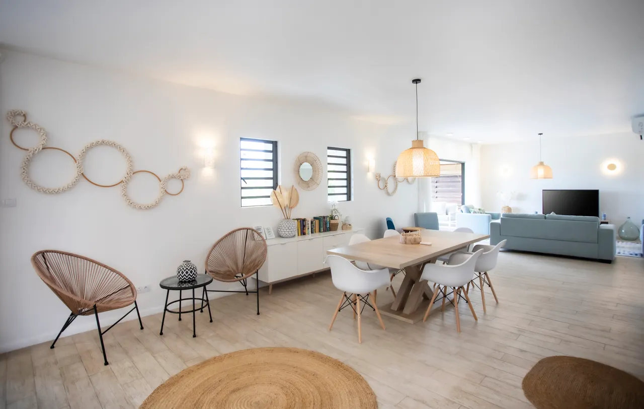 Salle à manger avec mobilier moderne et éclairage suspendu en osier.  
Espace ouvert offrant une circulation fluide entre les pièces.  
Sol en bois clair apportant une luminosité naturelle.  
Décor minimaliste et élégant contribuant à une ambiance sereine.  
Coin repas spacieux favorisant les moments conviviaux en intérieur.