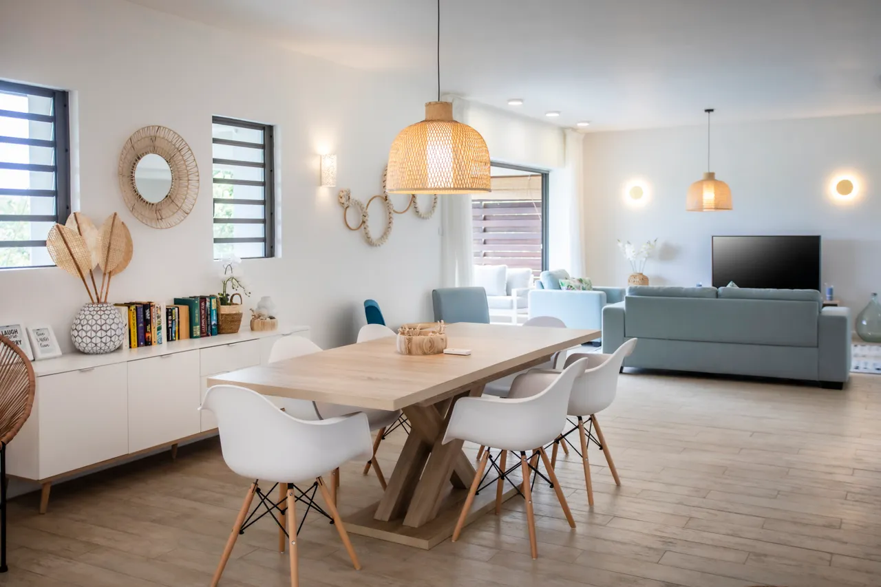 Sol en bois clair créant une ambiance lumineuse dans l'espace de vie.  
Mobilier moderne en bois ajoutant une touche contemporaine à la salle à manger.  
Éclairage suspendu en osier apportant une chaleur à l'intérieur.  
Espace ouvert favorisant la circulation entre le coin repas et le salon.  
Décor minimaliste et épuré créant une atmosphère sere