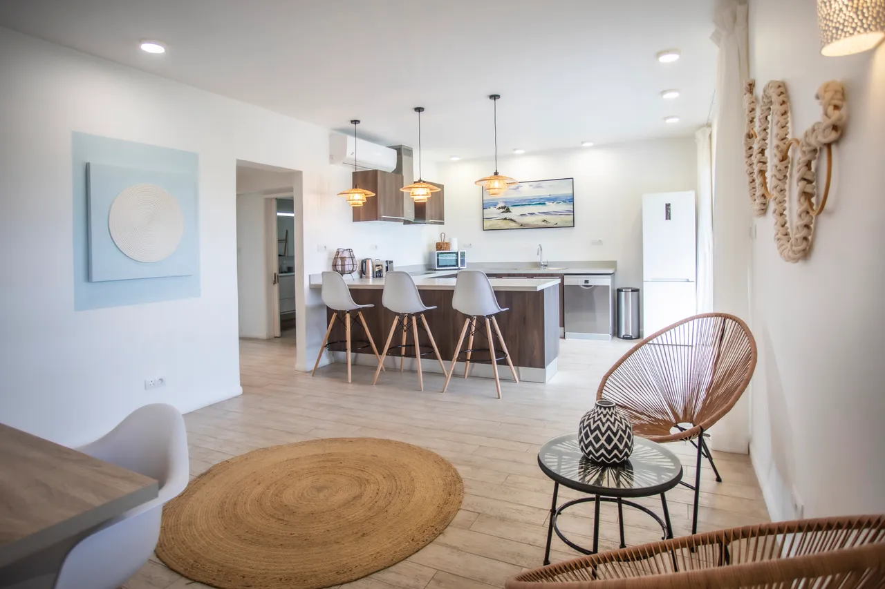 Lumière naturelle abondante grâce aux grandes fenêtres dans l'espace de vie.  
Mobilier moderne en bois ajoutant une touche contemporaine à la décoration.  
Coin repas intégré offrant un cadre agréable pour les repas en famille.  
Éclairage suspendu créant une ambiance chaleureuse et accueillante.  
Agencement ouvert favorisant une circulation fluide entre les différentes zones.
