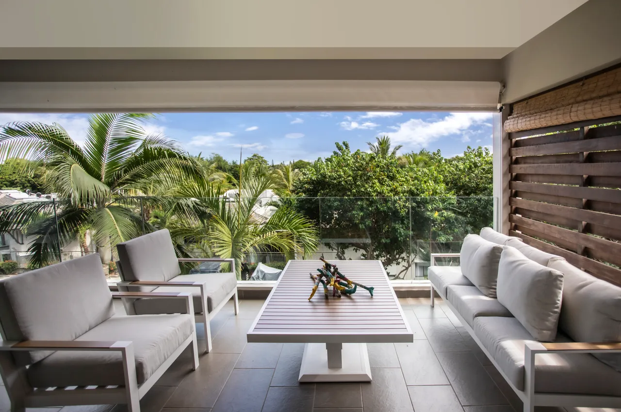 Espace extérieur avec mobilier confortable et vue sur la verdure environnante.  
Terrasse spacieuse propice à la détente en plein air.  
Vitrage transparent permettant une vue dégagée sur le jardin.  
Coin salon agréable pour profiter des journées ensoleillées.  
Accessibilité directe depuis le salon pour une fluidité d'utilisation.