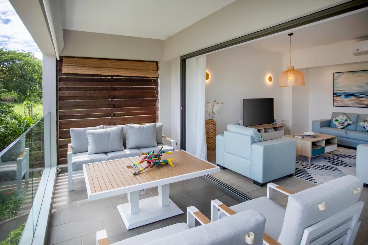 Espace de salon avec mobilier moderne et accès direct à l'extérieur.  
Terrasse avec table à manger offrant une vue sur le jardin.  
Grandes baies vitrées permettant une luminosité abondante dans la pièce.  
Éclairage suspendu en osier ajoutant une touche chaleureuse à l'espace.  
Agencement ouvert favorisant la circulation vers le coin salon.