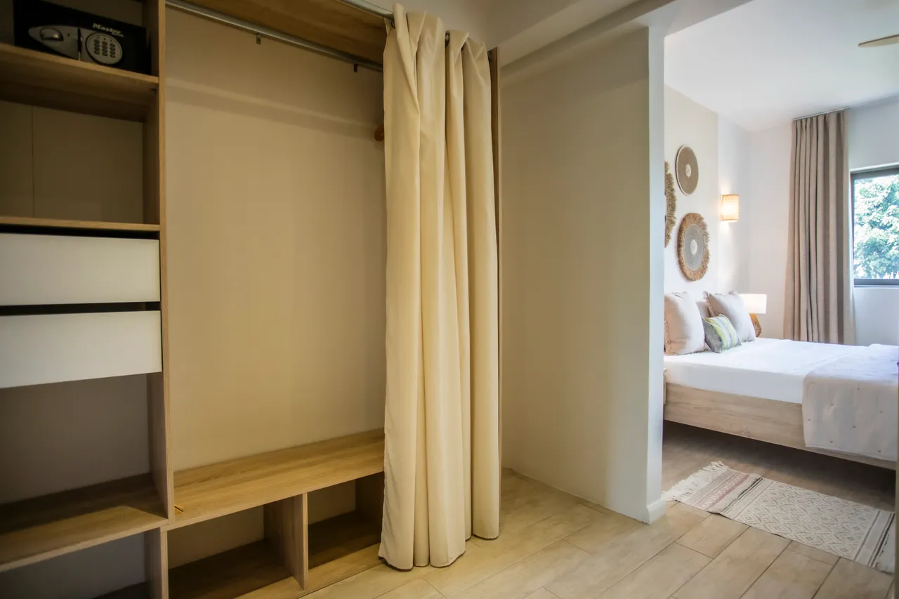 Espace de rangement intégré avec étagères et penderie.  
Tapis en textile doux ajoutant une touche de confort au sol.  
Cloison en rideau séparant le dressing de la chambre.  
Éclairage mural créant une ambiance douce dans la pièce.  
Finition en bois naturel pour un style contemporain.