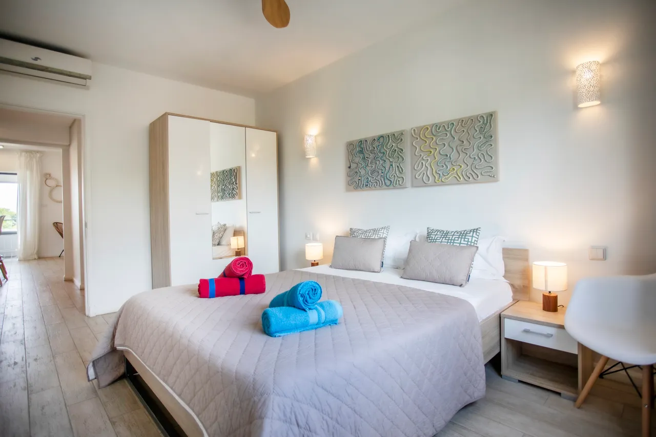 Chambre claire avec lit double et rangement intégré.  
Lumière naturelle et éclairage d'appoint pour un confort agréable.  
Textiles colorés ajoutant une touche de vie à l'espace.  
Sol en bois clair facilitant l'entretien quotidien de la pièce.  
Décoration murale sobre apportant une ambiance contemporaine.