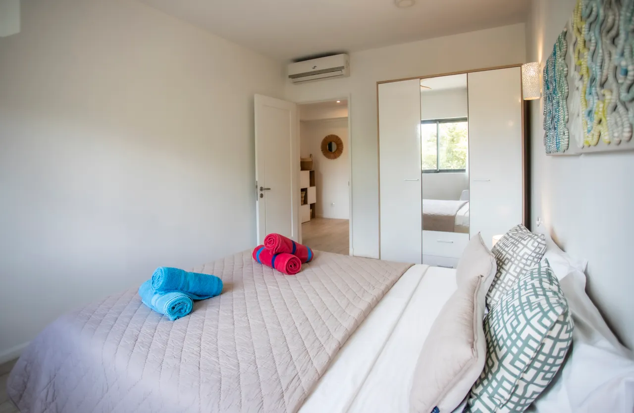 Chambre incluant lit double et rangement intégré pour un espace optimisé.  
Fenêtre apportant une lumière naturelle et une vue agréable sur l'extérieur.  
Éléments textiles colorés ajoutant de la variété à la décoration.  
Climatiseur pour un confort thermique durant les journées chaudes.  
Sol en carrelage clair facilitant l'entretien de la pièce.