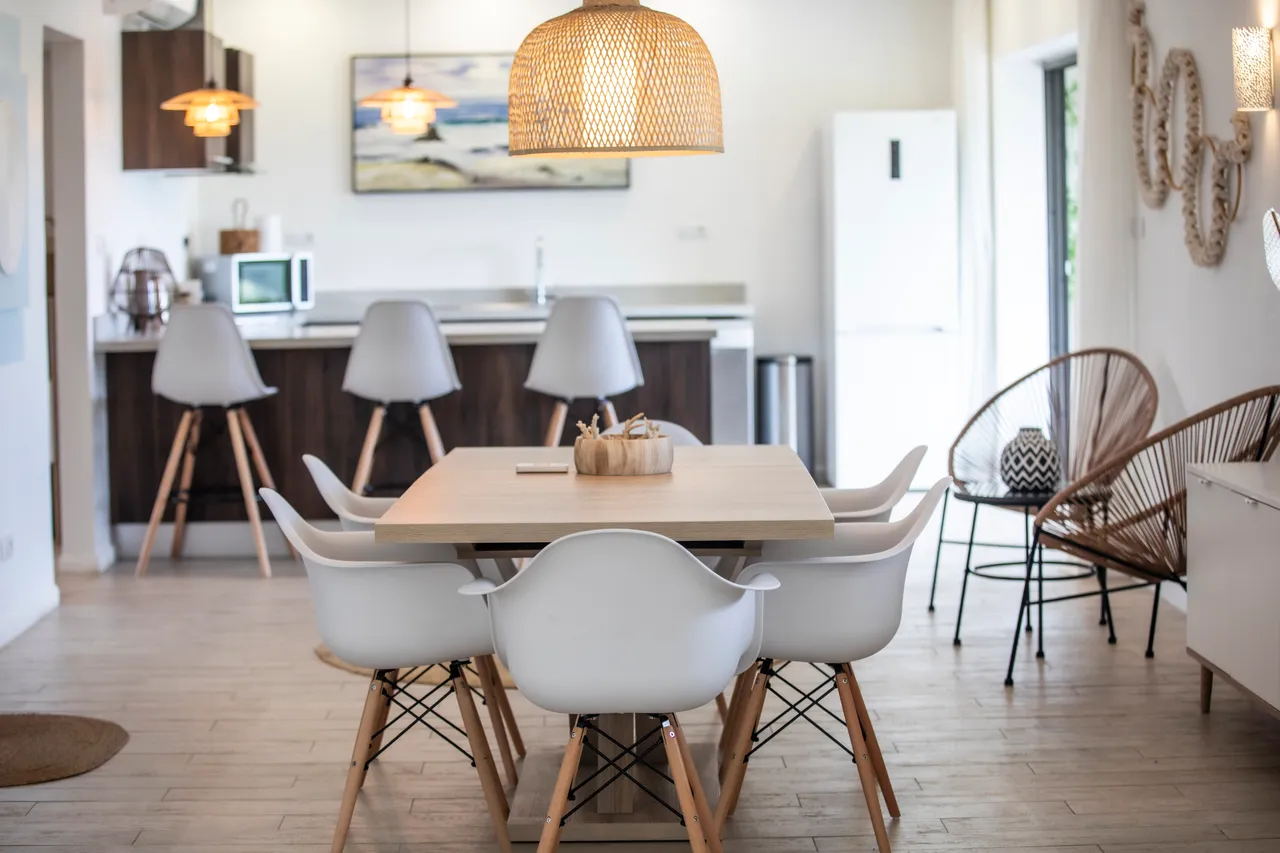 Salle à manger avec une table en bois et chaises contemporaines.  
Suspension en osier apportant une touche rustique à l'espace.  
Espace ouvert sur la cuisine, favorisant la convivialité.  
Éclairage naturel grâce aux fenêtres laissant entrer la lumière.  
Sol en bois clair facilitant l'entretien de la pièce.