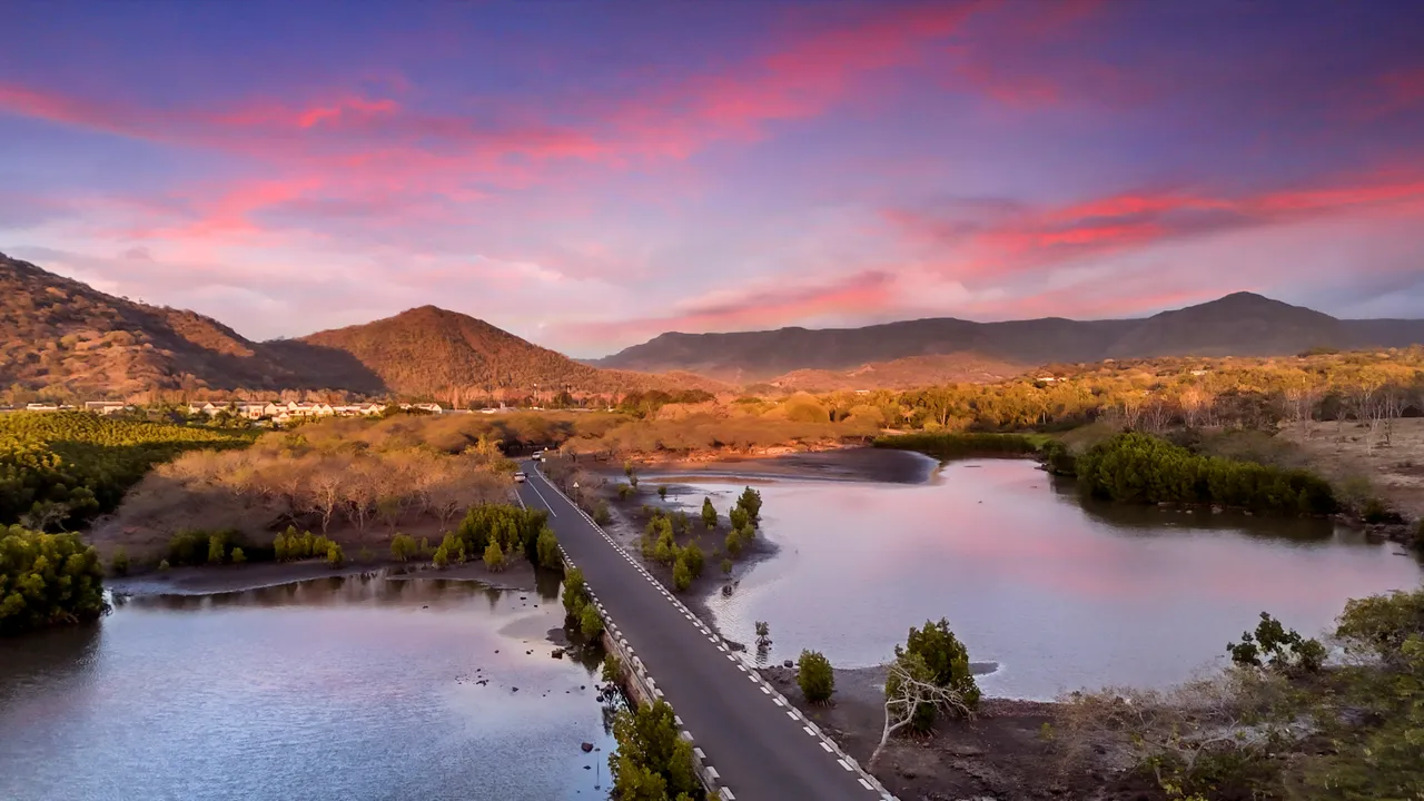 Vue aérienne d'un chemin bordé d'eau entouré de collines verdoyantes. Ciels colorés au crépuscule.