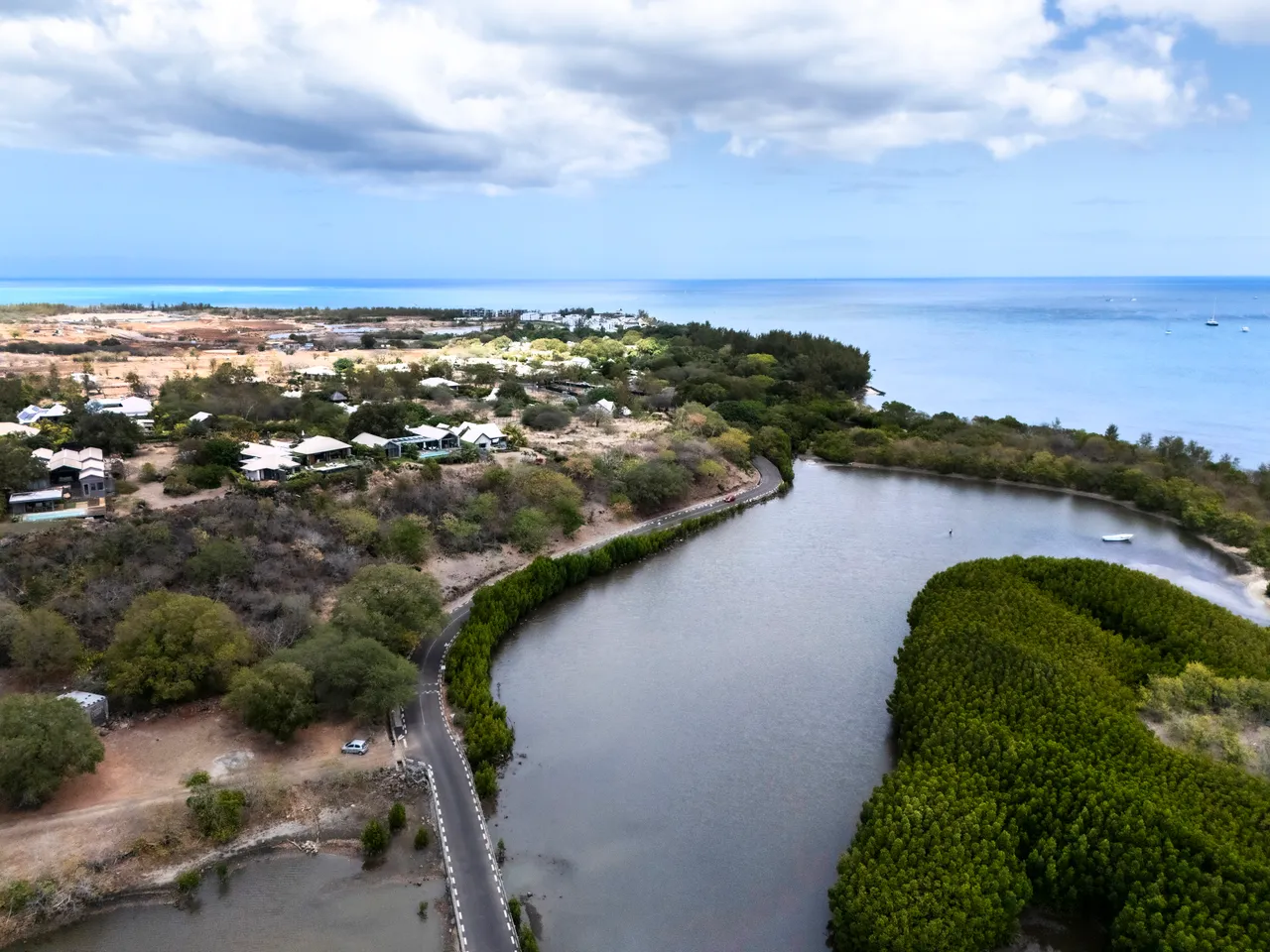 Vue aérienne d'une rivière sinueuse entourée d'une végétation dense et verdoyante. Le littoral se dessine au loin, offrant une perspective sur la mer.