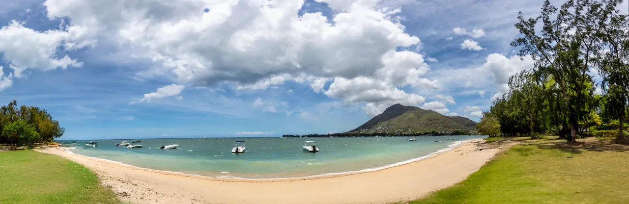 Plage de sable fin avec des bateaux amarrés près du rivage. Vue sur la montagne en arrière-plan.