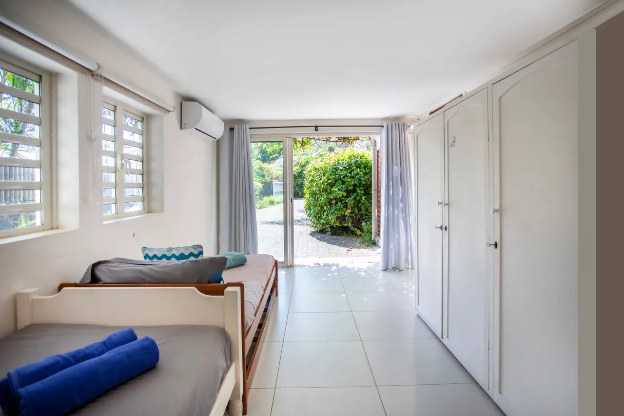 Chambre avec lits simples, fenêtres coulissantes donnant sur le jardin. Espace de rangement encastré et lumière naturelle.