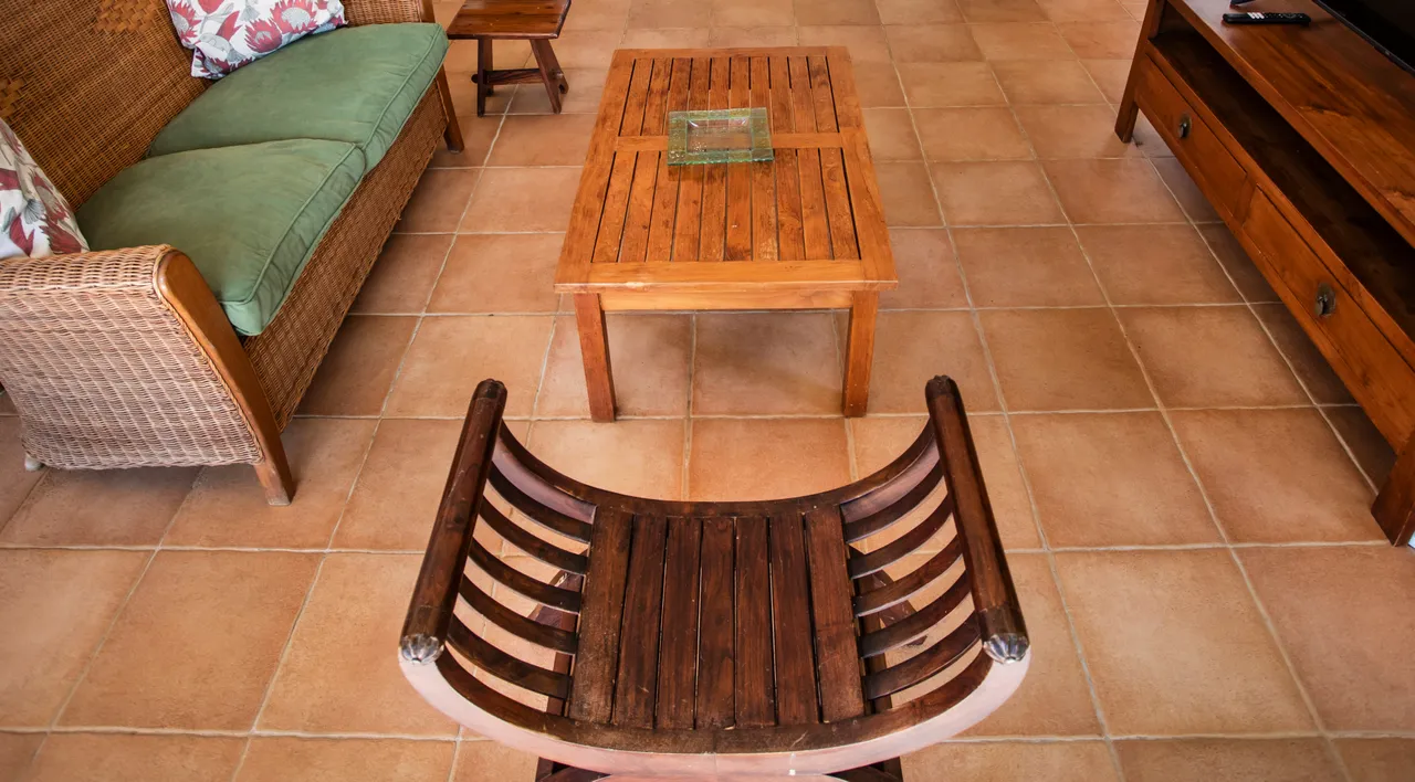 Galerie avec mobilier en rotin et table basse en bois. Espace lumineux avec sols en carrelage clair. Chaises en bois ajoutent une touche naturelle à l'agencement.
