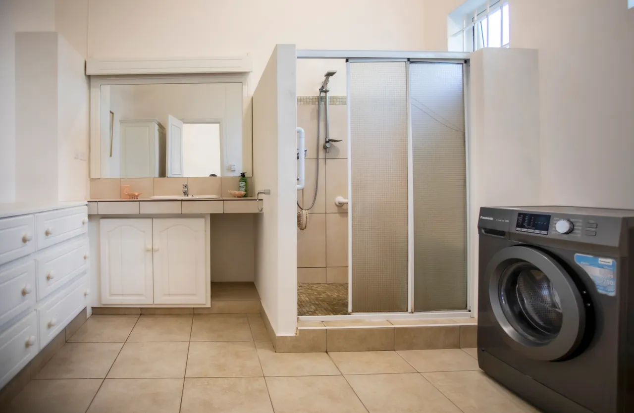 Salle de bain spacieuse avec douche et machine à laver intégrée. Éclairage naturel par fenêtres.