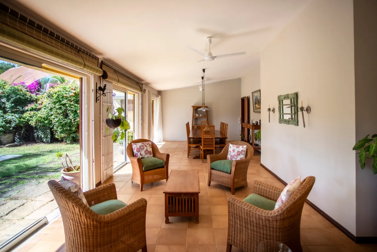 Sol en terre cuite avec mobilier en rotin dans un espace ouvert et lumineux. Accès direct au jardin depuis la galerie.