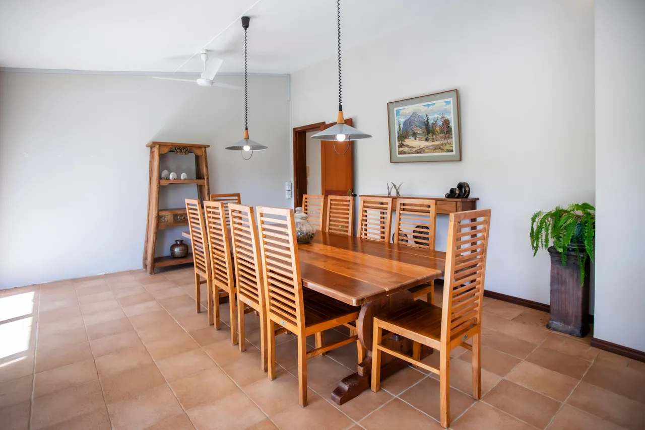 Salle à manger lumineuse avec grande table en bois et chaises en bois. Éclairée par des luminaires suspendus.
