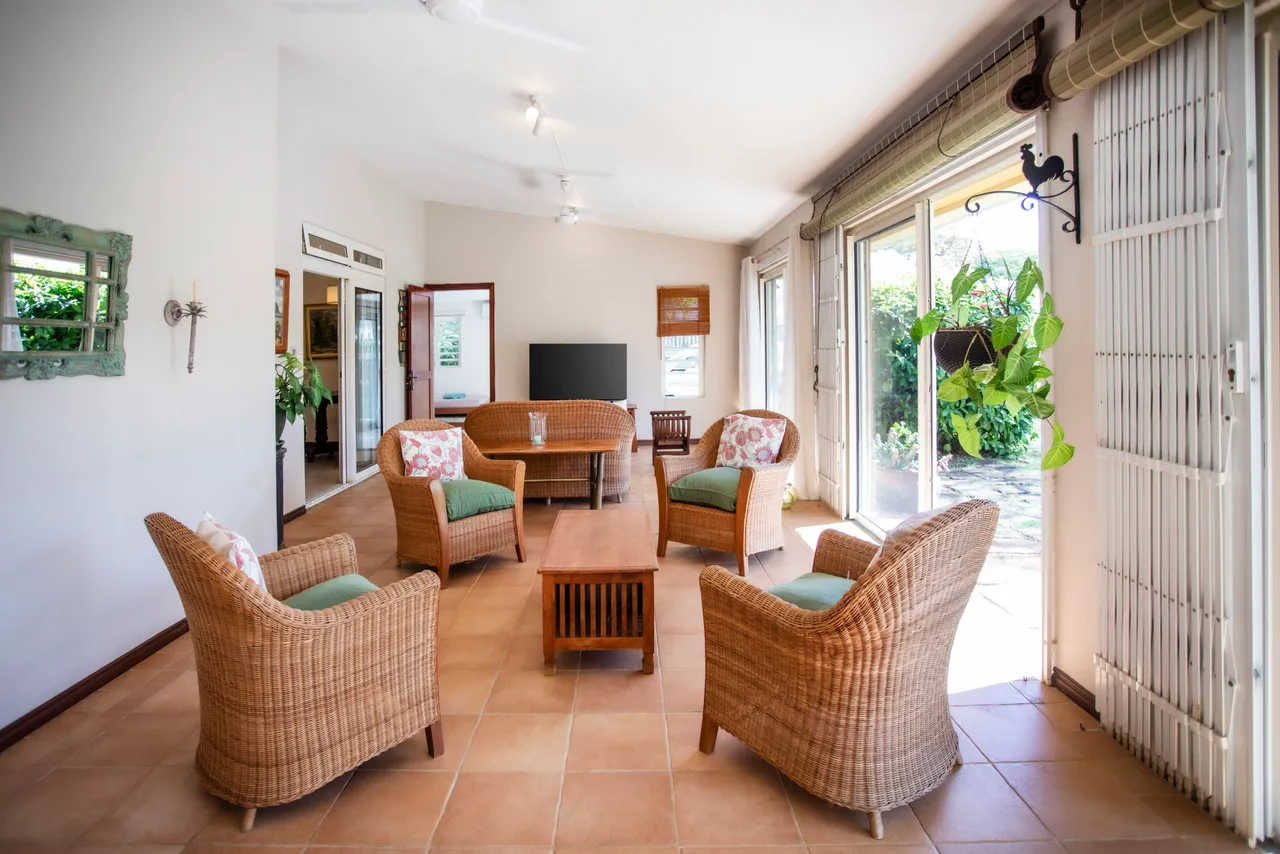 Espace salon avec fauteuils en rotin et table basse centrale. Accès direct au jardin par les baies vitrées.