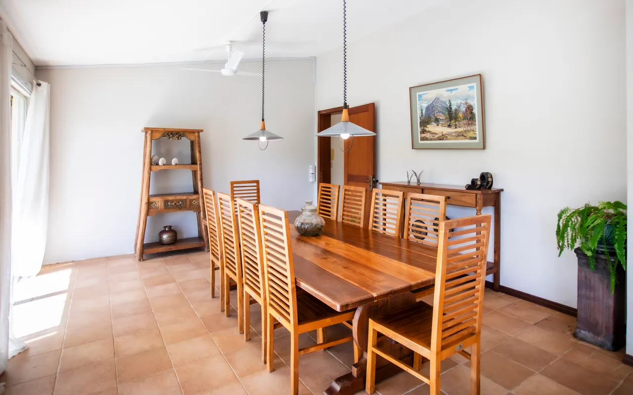 Table en bois massif entourée de chaises en bois dans un espace lumineux. Éclairée par des luminaires suspendus, cette galerie offre un accès direct au jardin.