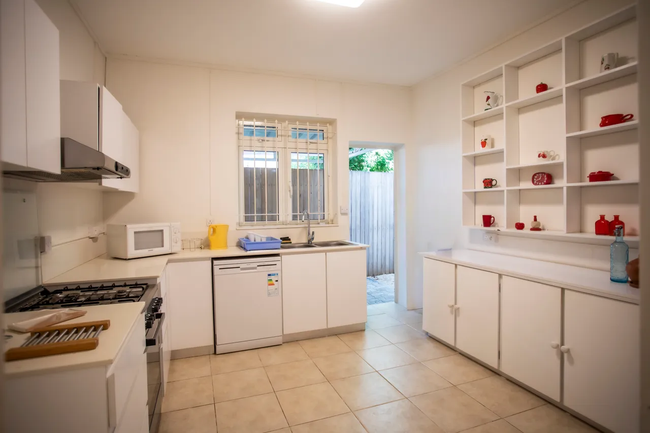Cuisine spacieuse avec rangements intégrés et plan de travail fonctionnel. Accès à l'extérieur par une porte. Équipements modernes tels qu'un four et un lave-vaisselle.