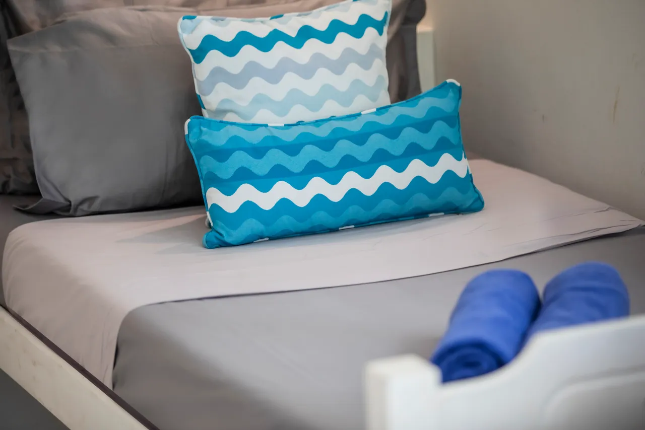 Teintes de bleu sur les coussins d'un lit simple, créant une ambiance sereine. Serviettes pliées offrent un aspect soigné.