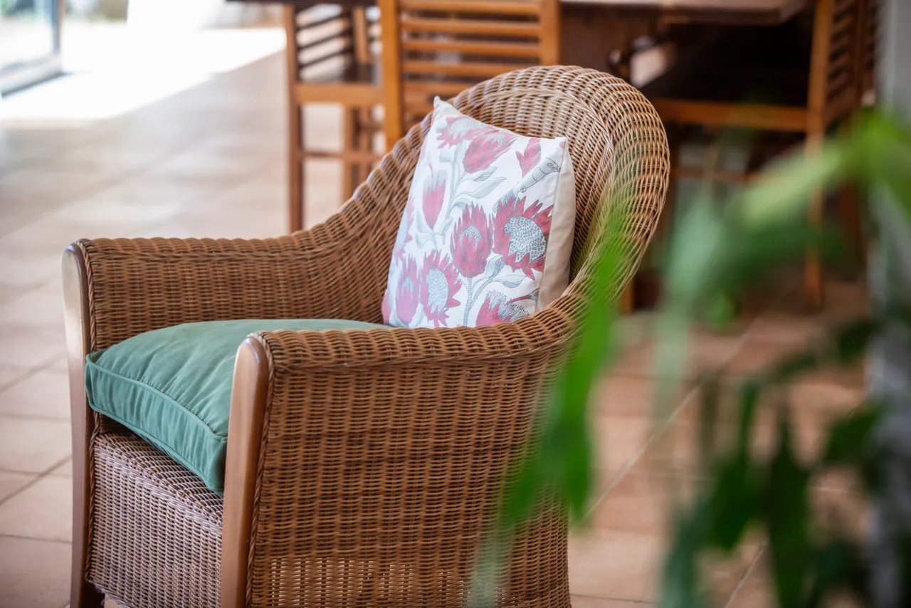 Fauteuil en osier avec coussin coloré, placé dans une galerie lumineuse.