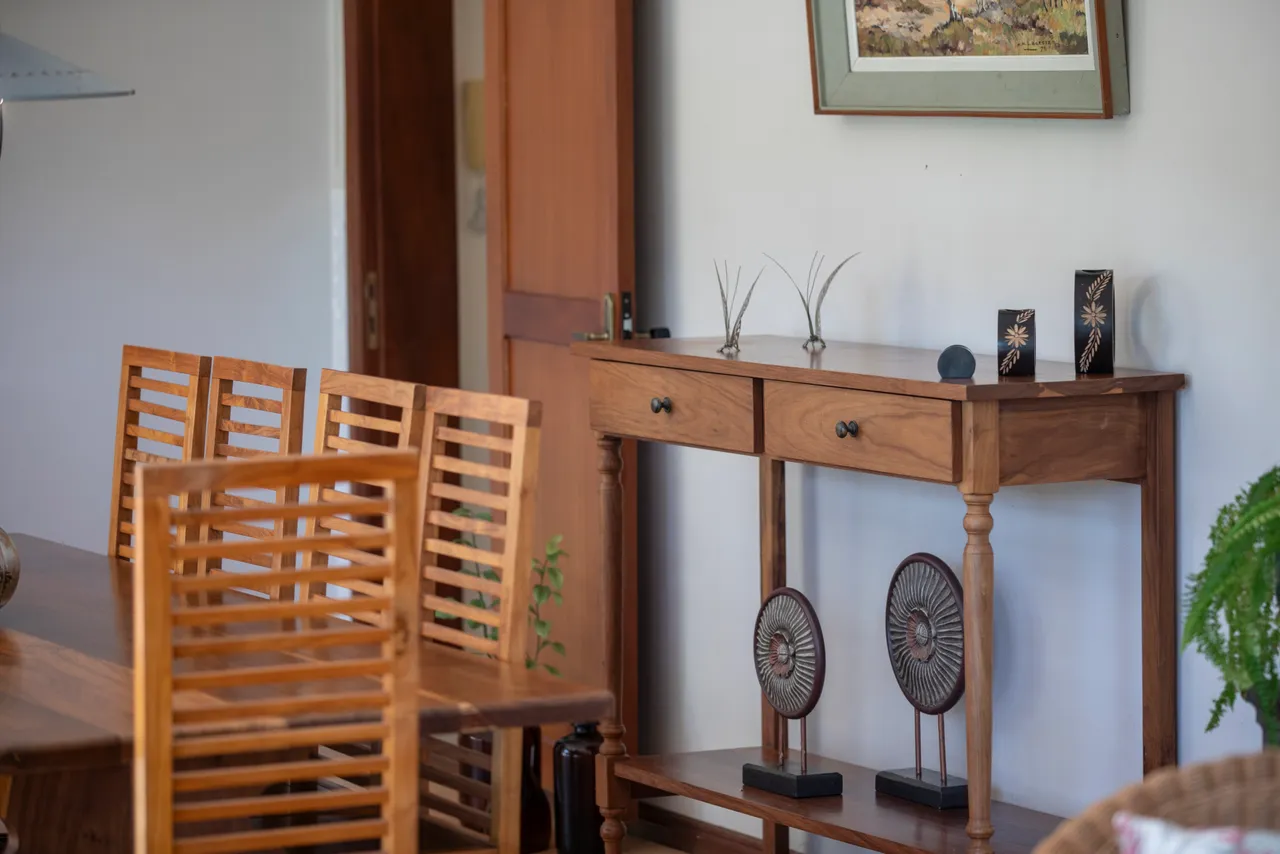 La galerie présente un meuble en bois avec des décorations minimalistes. Une table en bois est visible, accompagnée de chaises en lattes.