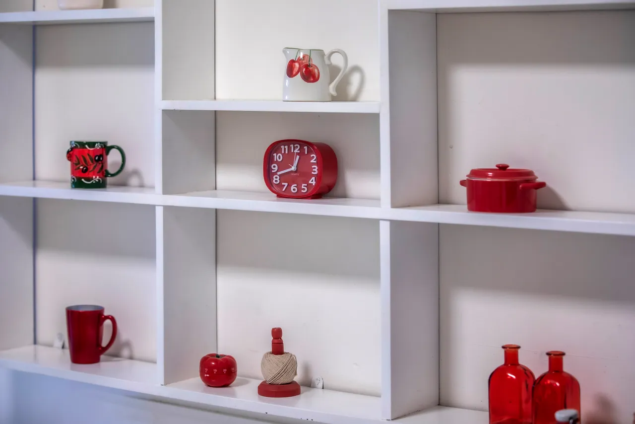 Étagère blanche contenant divers objets rouges, y compris des tasses et un réveil.