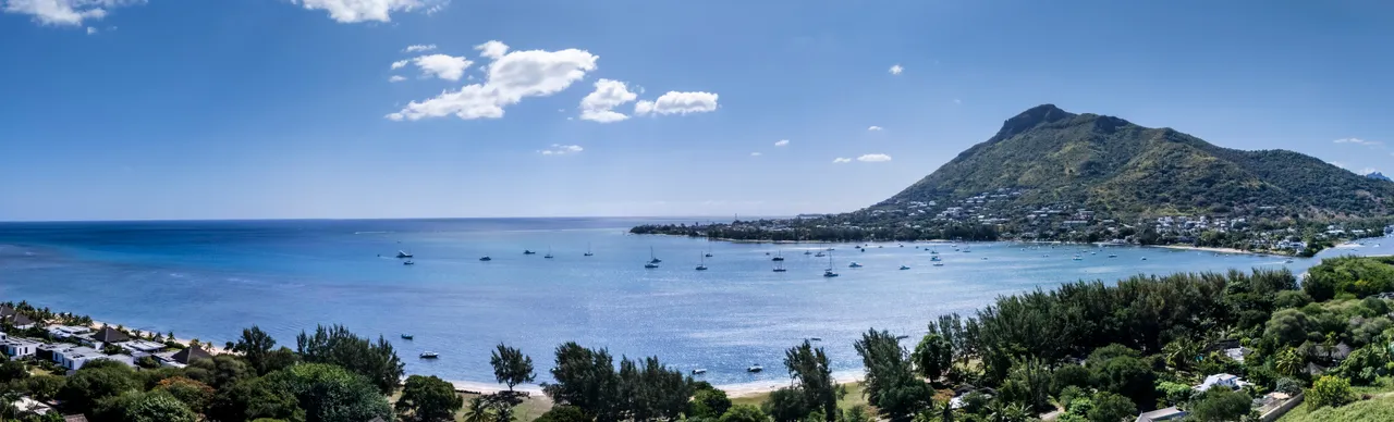 Vue panoramique sur la mer et la montagne, avec des bateaux au loin.