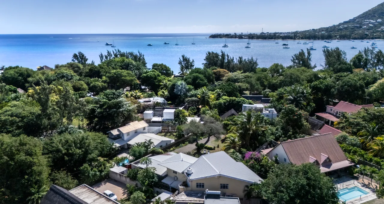 Vue dégagée sur la mer, entourée de végétation tropicale. Plusieurs habitations visibles depuis les hauteurs.