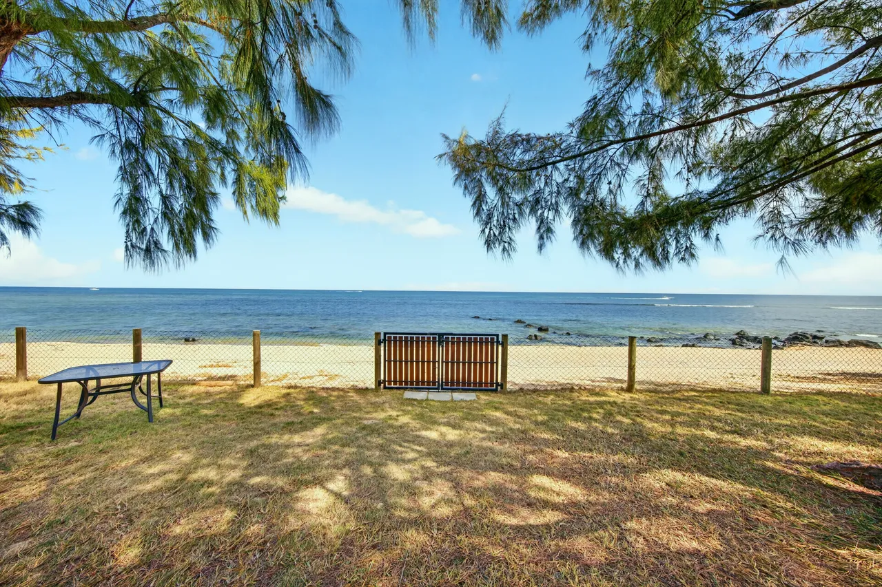 L’herbe ombragée s’étend jusqu’à une clôture basse, avec un banc face au lagon.
