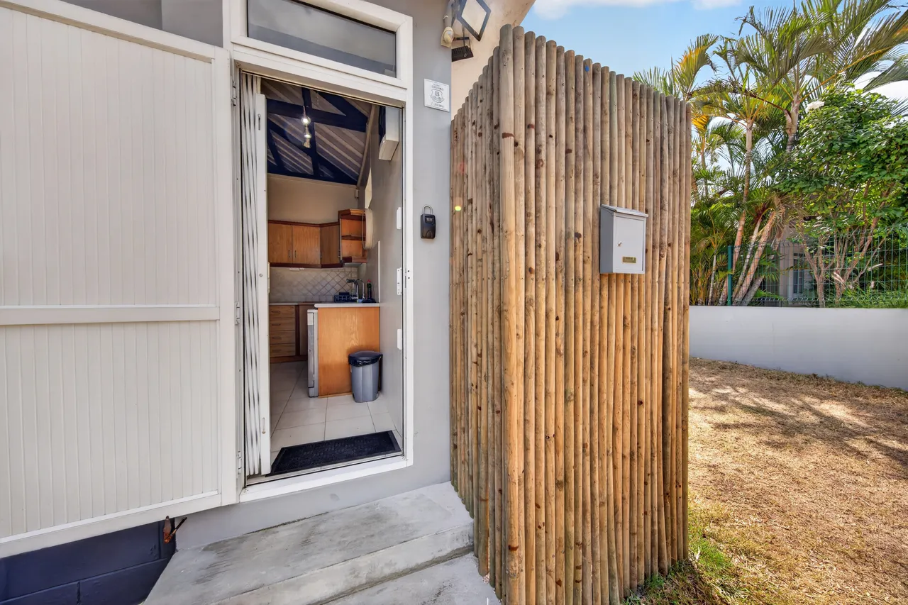 Façade en bois clair, une porte ouverte révèle l’entrée et la cuisine.