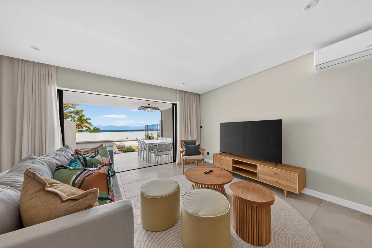 Beige et bois clair dominent le salon, ouvert sur une terrasse avec vue sur mer.