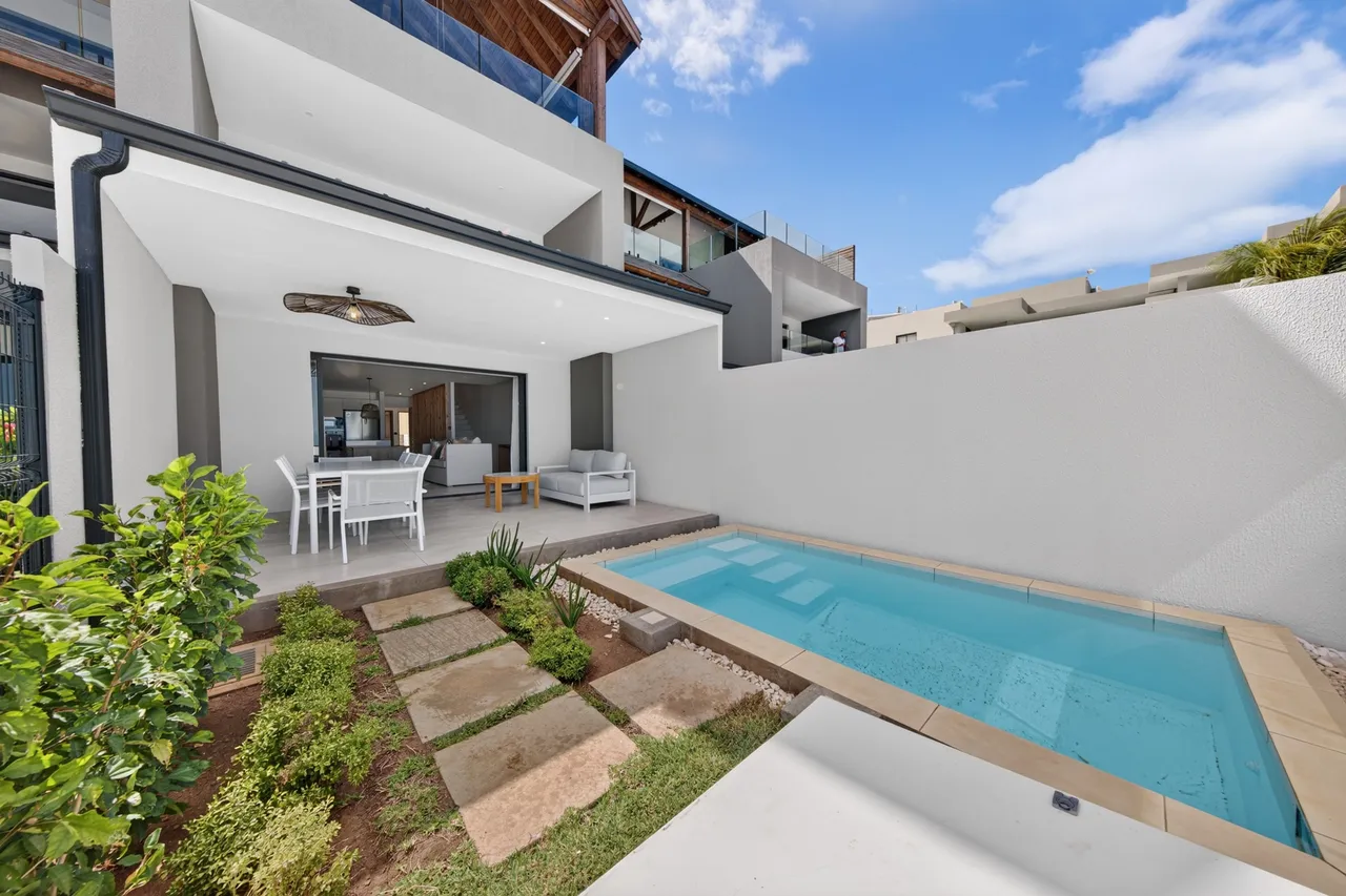 Une piscine rectangulaire longe la terrasse aménagée devant les baies vitrées.
